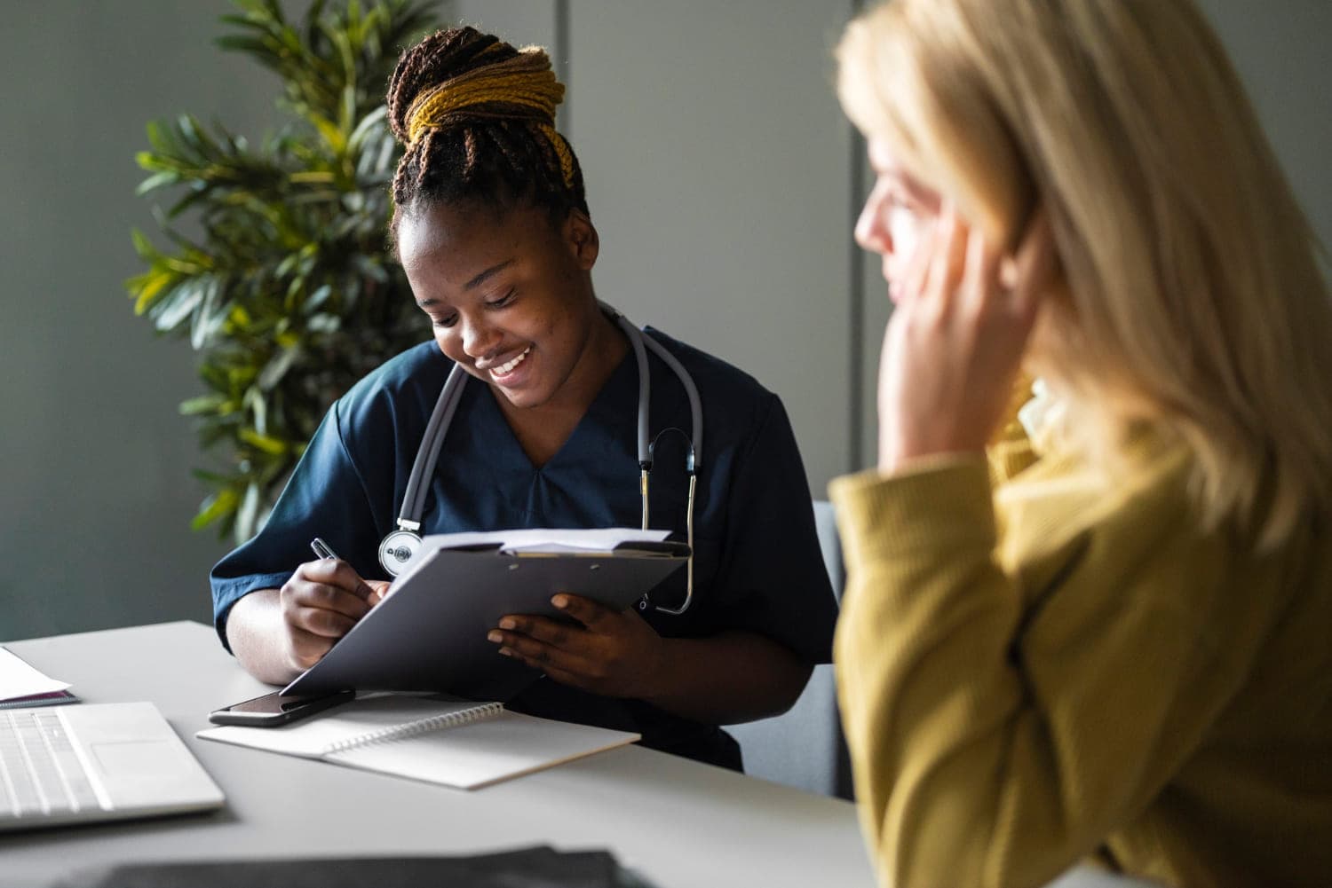Smiling clinician taking notes on a clipboard while talking with a patient