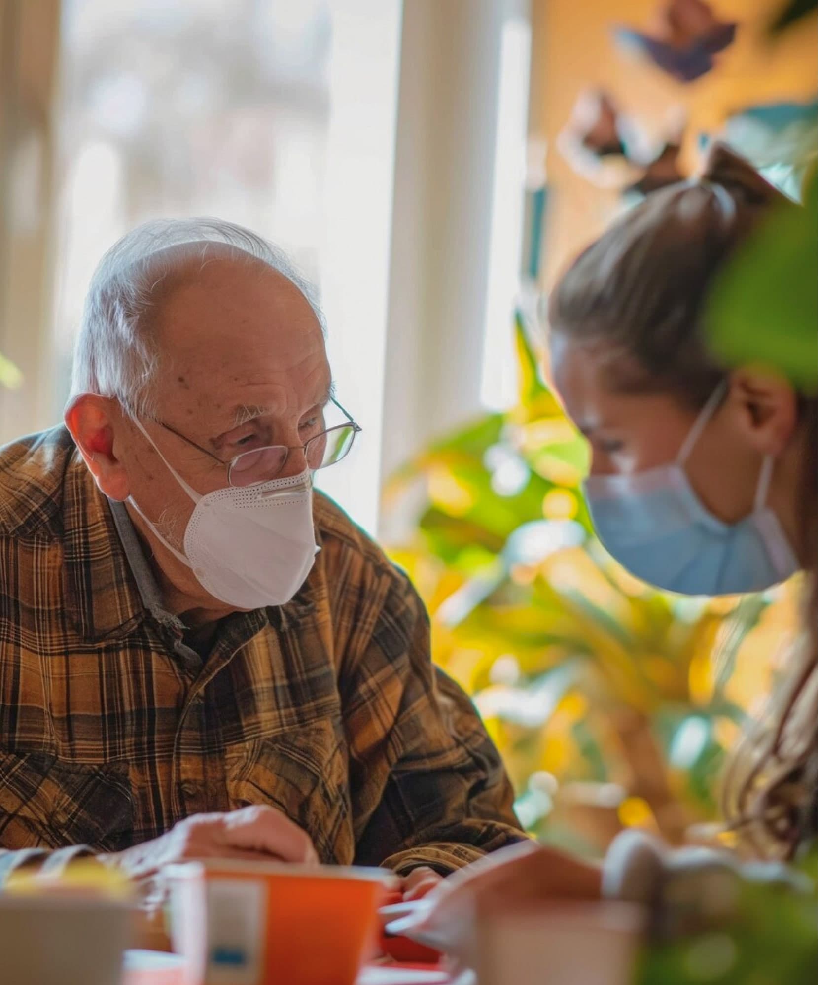 Older man in a mask with a caregiver at the table