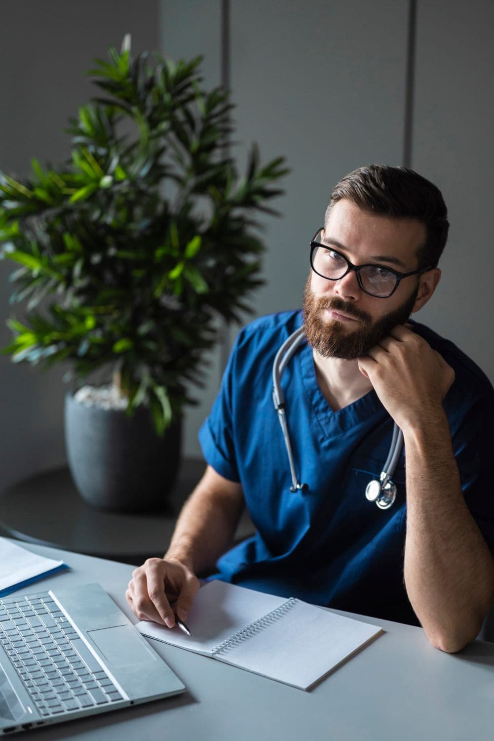Physician in scrubs and glasses listening thoughtfully at his desk